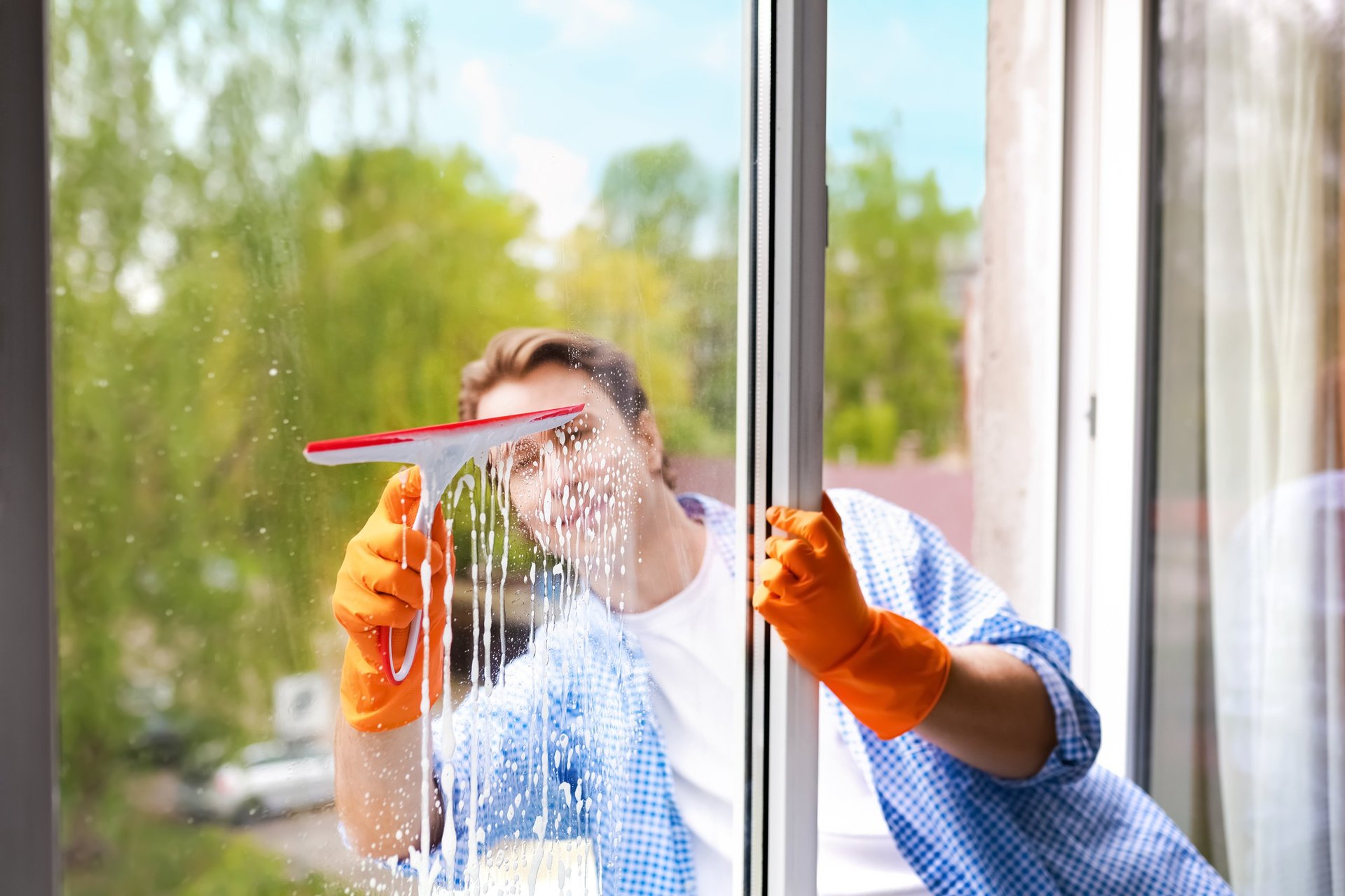 Smiling man doing housework by washing a glass window with a squeegee and soapy water